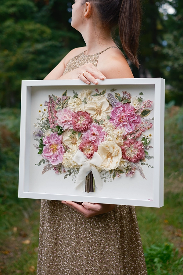 Končni izdelek s klasično razporeditvijo cvetov v zlatem okvirju in med dvema stekloma.  Poročni šopek so sestavljale bele vrtnice, rožnati liziantusi, evkaliptus in šlajer.